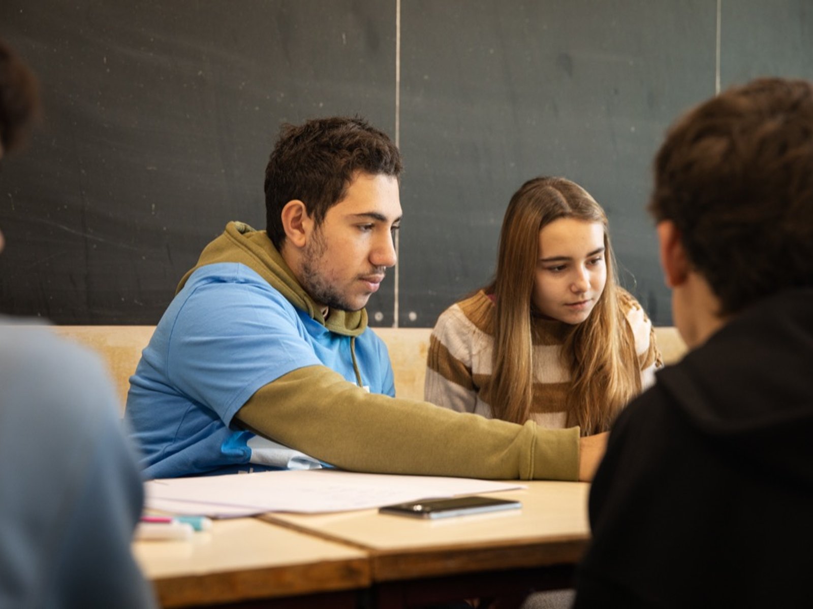 Um instrutor Alpha trabalha à mesa com uma aluna e outros participantes.
